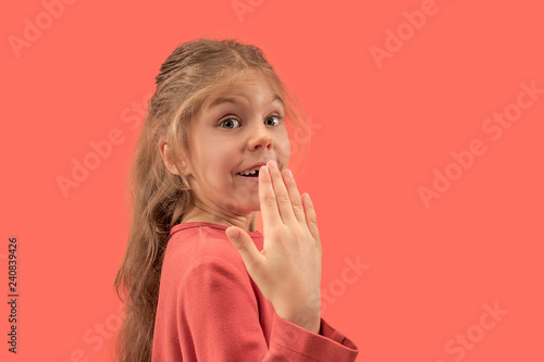 Cute happy little surprised girl in coral dress with long hair looking to camera at studio. Human emotions and facial expression over trendy color