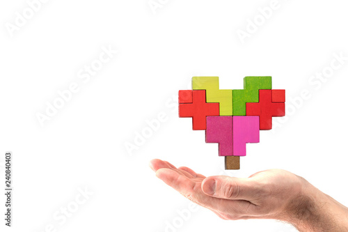Human hand holding abstract heart. Human heart is made of multi-colored wooden blocks.