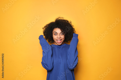 Portrait of excited African-American woman on color background © Pixel-Shot