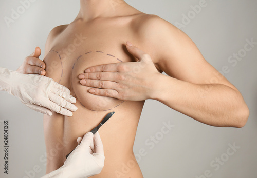 Naked woman and doctor with lancet on grey background. Concept of breast augmentation photo