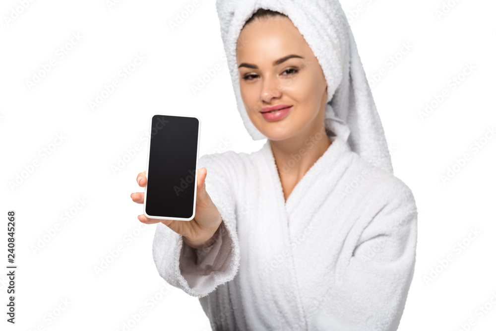 attractive girl in bathrobe with towel on head showing smartphone and looking at camera isolated on white attractive girl in bathrobe with towel on head showing smartphone and looking at camera isolated on white