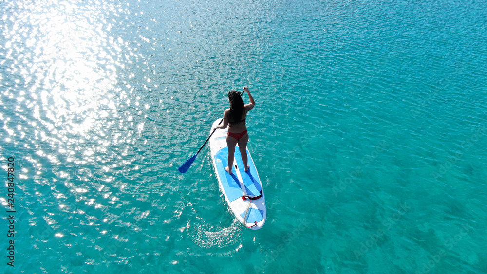 Aerial photo of fit woman practising SUP or Stand Up Paddle Board in tropical exotic sandy beach with emerald clear sea