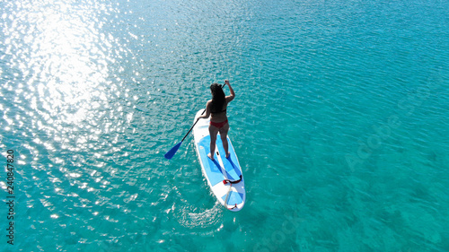 Aerial photo of fit woman practising SUP or Stand Up Paddle Board in tropical exotic sandy beach with emerald clear sea