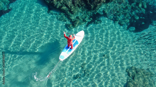Aerial photo of fit man dressed as Santa Claus practising SUP or Stand Up Paddle in exotic mediterranean beach with turquoise sea © aerial-drone