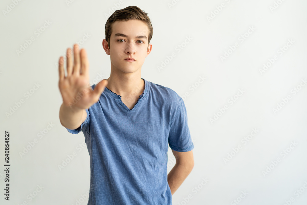 Serious strict young man making restriction gesture and looking at camera. Handsome guy showing stop gesture. Limitation concept Serious strict young man making restriction gesture and looking at camera. Handsome guy showing stop gesture. Limitation concept
