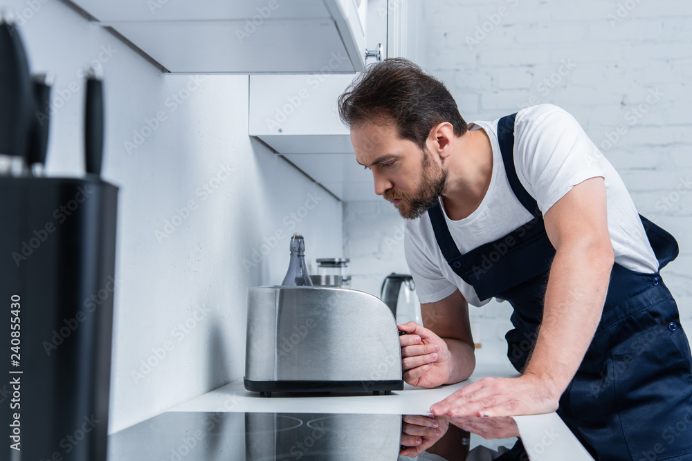 serious handyman in working overall fixing toaster in kitchen serious handyman in working overall fixing toaster in kitchen