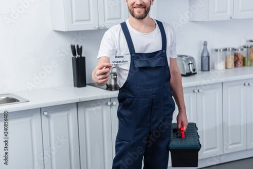 partial view of male handyman holding toolbox and showing card with lettering home inspection