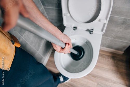 cropped shot of male plumber using plunger and cleaning toilet in bathroom