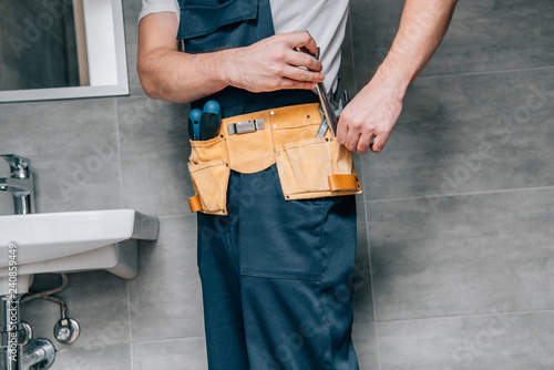 cropped shot of male plumber putting wrench in toolbelt in bathroom photo