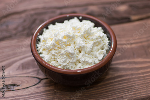 Cottage cheese in a plate on a wooden background.
