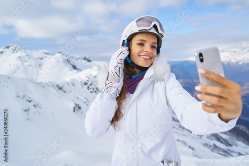 Woman skier making selfie photo on the background of snowy high mountains and