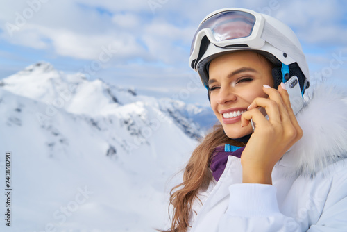 Attractive young woman at a mountain ski resort. Standing on a snow chatting on her mobile phone and laughing