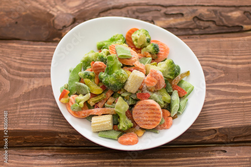Frozen various vegetables on a plate on a wooden background.