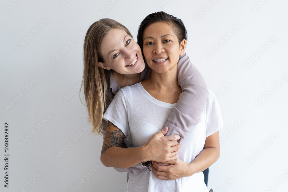 Cheerful women embracing and looking at camera. Diverse homosexual couple. Lesbian couple concept. Isolated front view on white background. Cheerful women embracing and looking at camera. Diverse homosexual couple. Lesbian couple concept. Isolated front view on white background.
