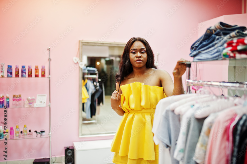 Stylish african american woman at yellow dreess posed at pink shop and chooses clothes. Stylish african american woman at yellow dreess posed at pink shop and chooses clothes.