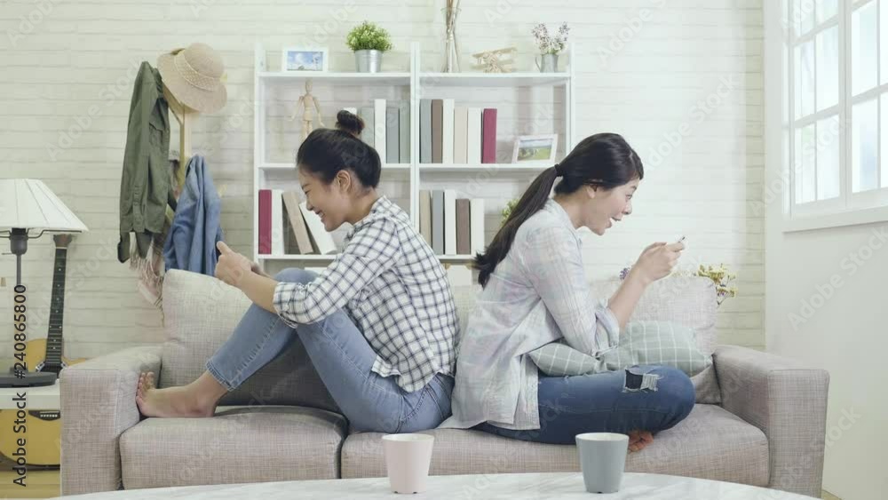 slow motion of two excited girls touching finger fast on screen playing games on cellphone. young ladies having online competition on mobile sitting back to back in car racing app. friends enjoy life slow motion of two excited girls touching finger fast on screen playing games on cellphone. young ladies having online competition on mobile sitting back to back in car racing app. friends enjoy life