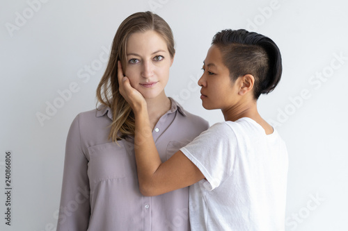 Serious Asian woman touching girlfriend face. Diverse homosexual couple. Lesbian couple concept. Isolated front view on white background.