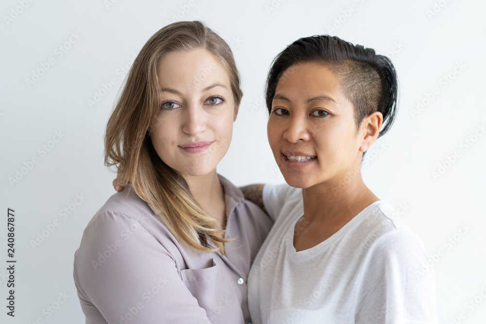 Smiling lesbian couple embracing and looking at camera. Multiethnic homosexual couple. Lesbian couple concept. Isolated front view on white background. Smiling lesbian couple embracing and looking at camera. Multiethnic homosexual couple. Lesbian couple concept. Isolated front view on white background.