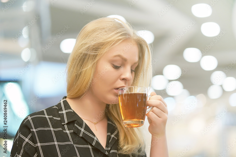 A young girl drinks tea in a cafe. Blonde enjoying hot tea. Portrait of a young woman drinking her morning teaover a breakfast in the cafe. Toning A young girl drinks tea in a cafe. Blonde enjoying hot tea. Portrait of a young woman drinking her morning teaover a breakfast in the cafe. Toning