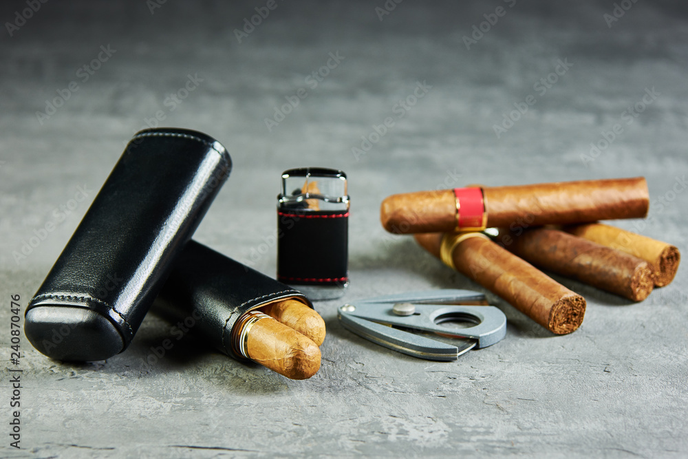 Six Cuban cigars on a stone table with a lighter, cutter and a leather case