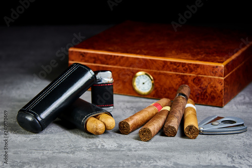 Six Cuban cigars on a stone table with a lighter, cutter and a wooden humidor and leather case.