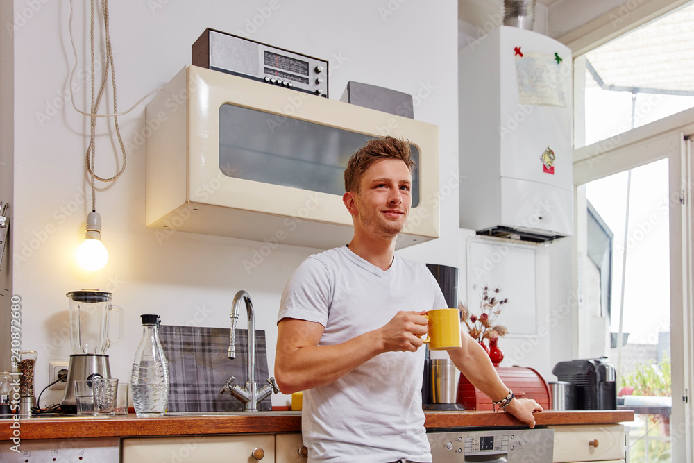 Smiling young man at home having a coffee break in kitchen Smiling young man at home having a coffee break in kitchen