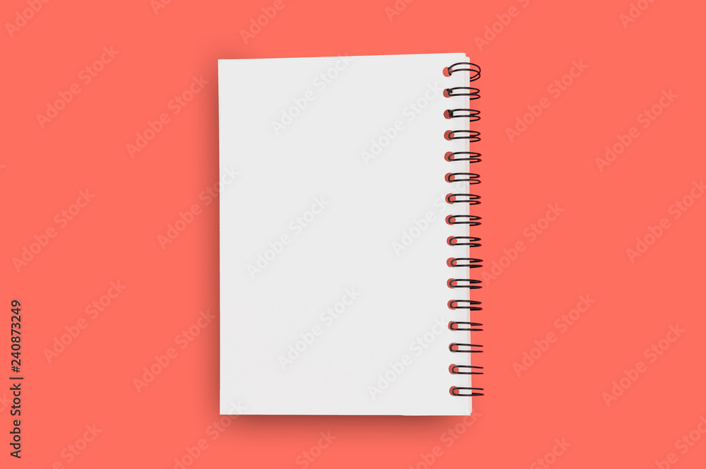 Blank paper notepad with spiral wire for note or drawing in center on background of living coral color. Copy space for your text. Business or education or other concept Blank paper notepad with spiral wire for note or drawing in center on background of living coral color. Copy space for your text. Business or education or other concept
