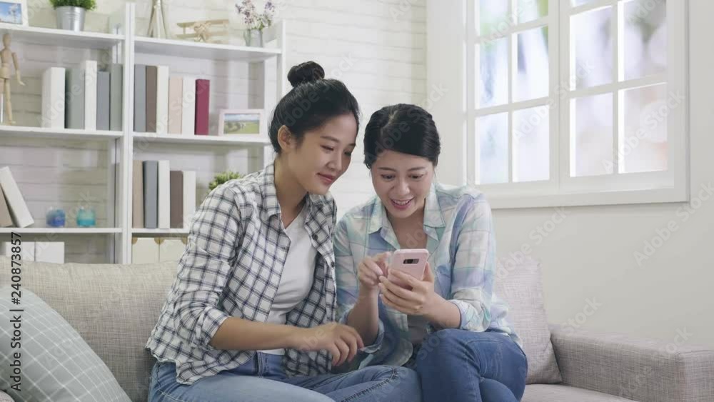 slow motion of sisters using smartphone touching screen watching funny video laughing cheerfully. young ladies shopping on christmas sale online store by mobile at home sitting on comfortable sofa. slow motion of sisters using smartphone touching screen watching funny video laughing cheerfully. young ladies shopping on christmas sale online store by mobile at home sitting on comfortable sofa.