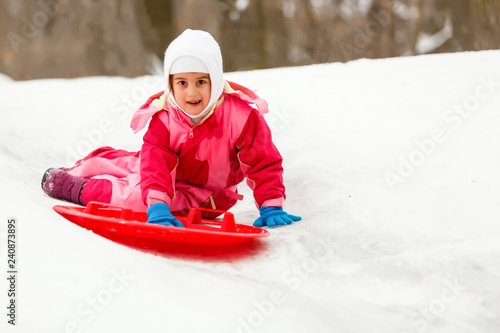 Cute little girl sliding down from the hill top covered with white and fluffy snow. One of the children favorite activity in winter time.