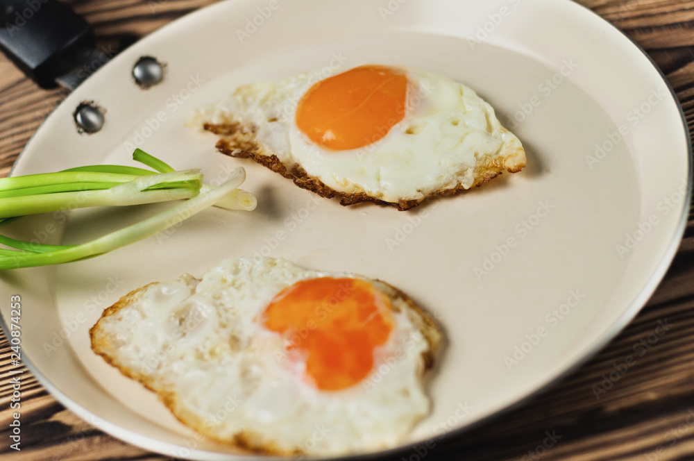 Two fried eggs in metal beige pan and green fresh onion on old wooden brown table Two fried eggs in metal beige pan and green fresh onion on old wooden brown table