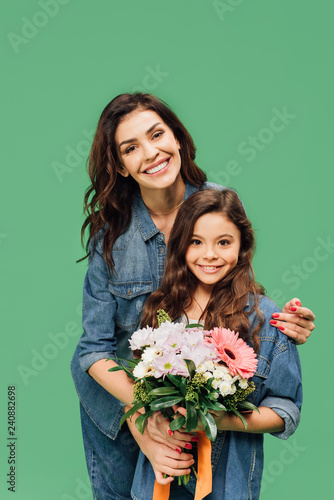 smiling mother embracing daughter with flower bouquet isolated on green