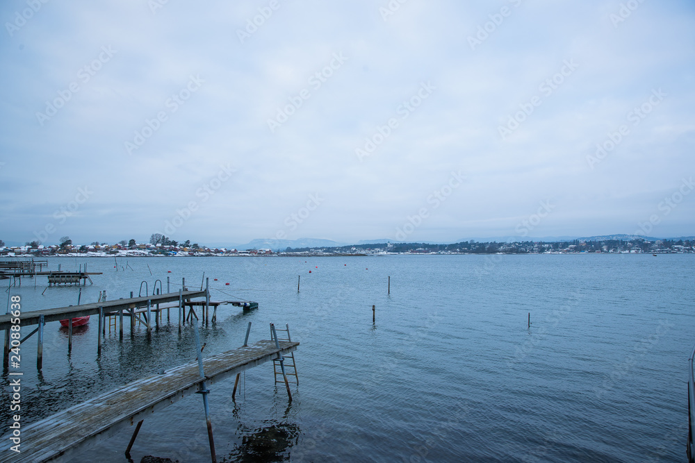 A pier for boats traveling between the Islands around Oslo Norway during the winter overlooking the sea and the Fjord covered by snow