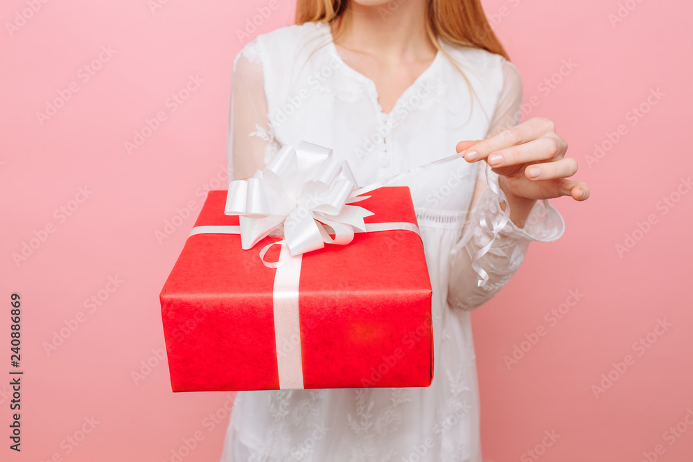A curious girl in a white dress with a gift box in her hand, wants to see what is in the box, on a pink background Valentine's Day A curious girl in a white dress with a gift box in her hand, wants to see what is in the box, on a pink background Valentine's Day