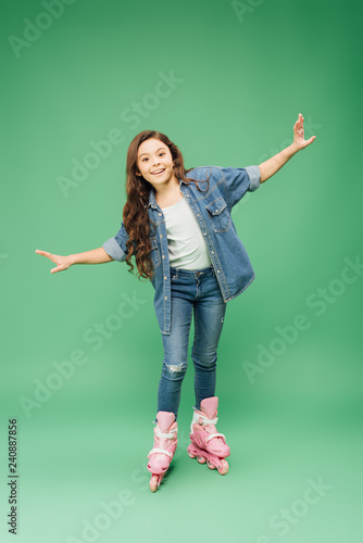 happy child rollerblading with outstretched hands on green background
