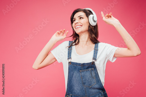 happy woman listening music in headphones isolated on pink