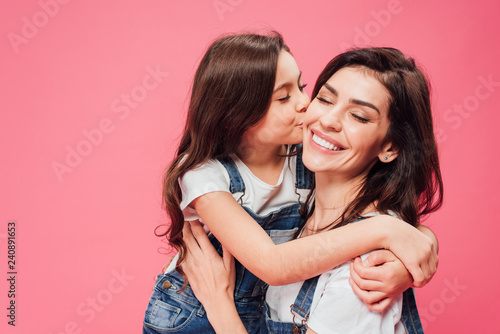 daughter kissing happy mother isolated on pink photo