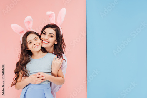 Canvas Print beautiful woman in easter bunny ears hugging child and looking at camera on blue