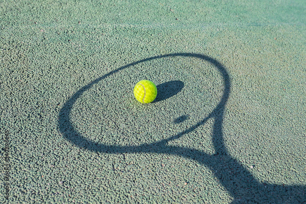 Tennis ball and shadow from racket on a green tennis hard court