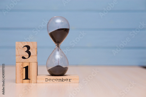 December 31st set on wooden calendar and hourglass with blue background.