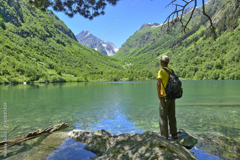 Tourist stands on the shore of the lake and looks at the mountains.