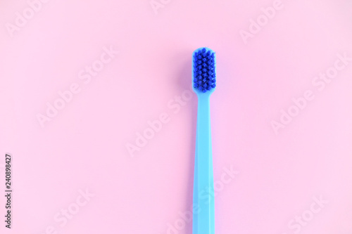 One blue toothbrush with blue bristle on pink background. Toothbrush for personal routine morning  hygiene on neutral blurred backdrop. Dental plastic tool with empty space for text or image