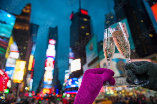 Gloved hands holding up Champagne glasses in a Mew Year’s Eve toast against the bright lights of Times Square, New York City