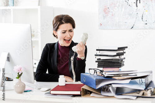 angry attractive businesswoman screaming while talking by stationary telephone in office
