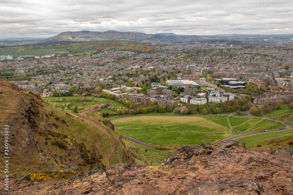 Urban landscape of Edinburgh in Scotland, as seen from Arthur's Seat peak. Cityscape on a Spring day with distant green hills and cherry blossom trees.