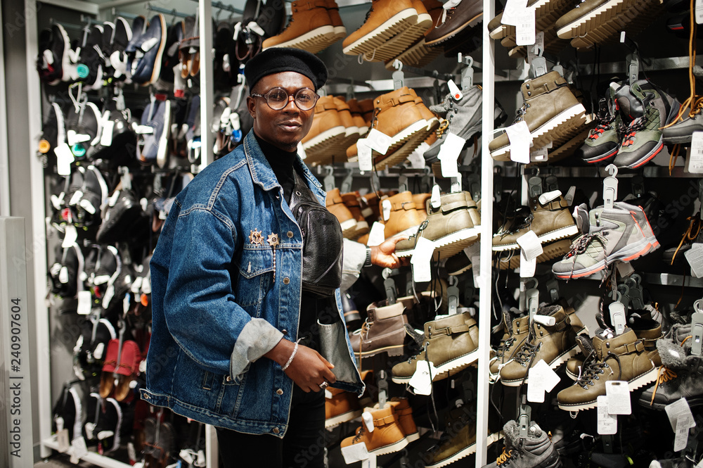 Stylish casual african american man at jeans jacket and black beret at clothes store trying new footwear.