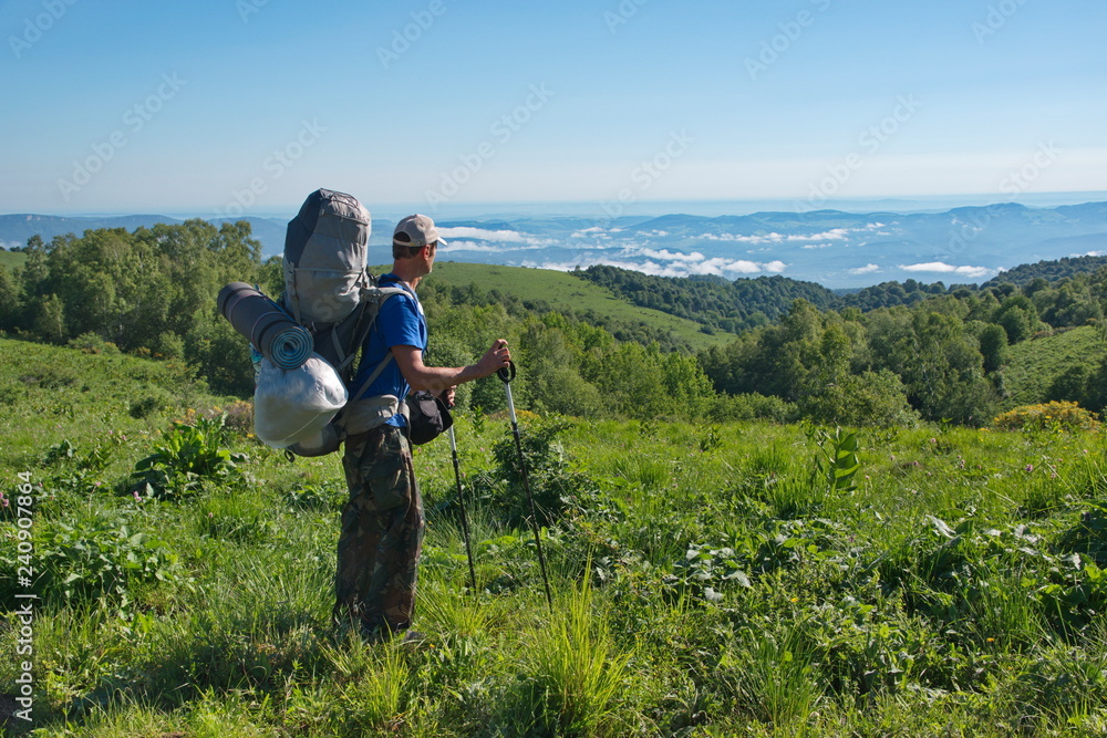 A man with a huge backpack is standing and looking at a mountain valley.