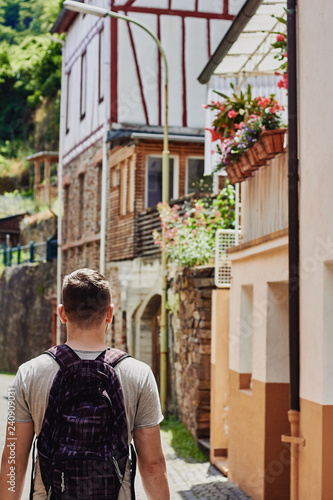 Young man traveler is walking along the narrow paved street with medieval houses © Olesia