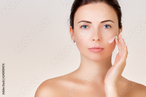 Portrait of a beautiful young woman. Facial care. Girl applies cream to face