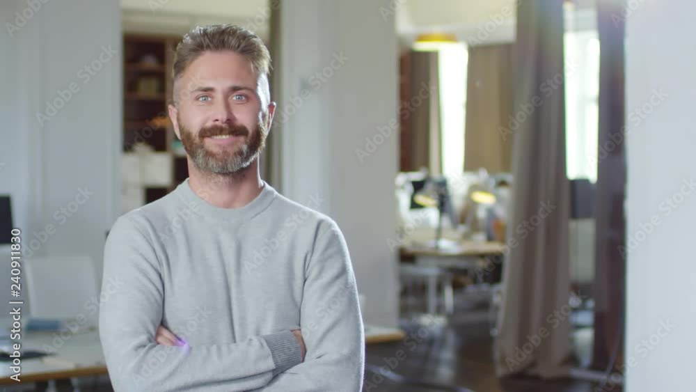 Tracking medium shot of cheerful bearded Caucasian businessman standing with crossed arms and smiling at camera Tracking medium shot of cheerful bearded Caucasian businessman standing with crossed arms and smiling at camera