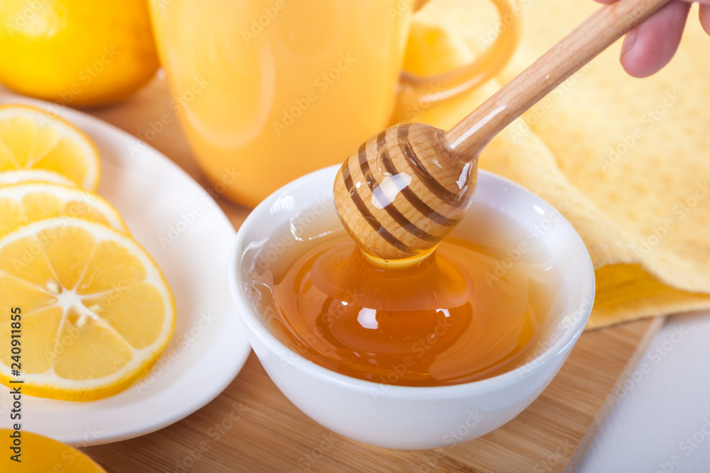 honey in a white ceramic bowl with honey dipper and lemon on a wooden kitchen boar honey in a white ceramic bowl with honey dipper and lemon on a wooden kitchen boar